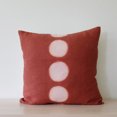 Hand dyed itajime kamppinen moon rust throw pillow with 5 undyed circles down middle on bench 