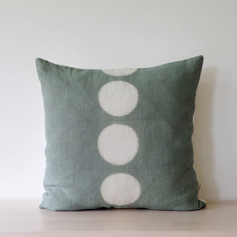 Sage handdyed hemp linen 18" square pillow with 5 undyed circles in vertical center line. Sits on bench. Handmade by kamppinen